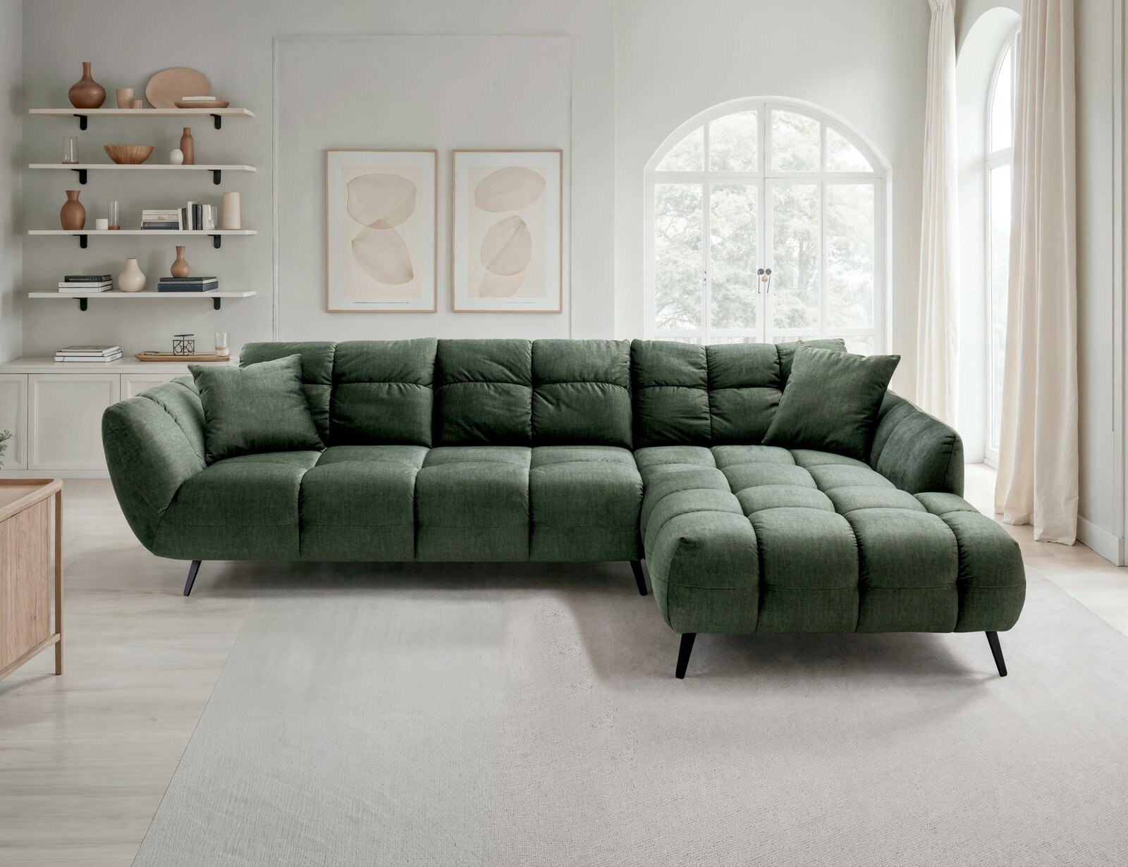 Grünes, gepolstertes Ecksofa mit Stepp-Optik und rechter Ottomane auf schwarzen Metallfüßen in hellem Wohnzimmer, Frontansicht leicht schräg von vorn.