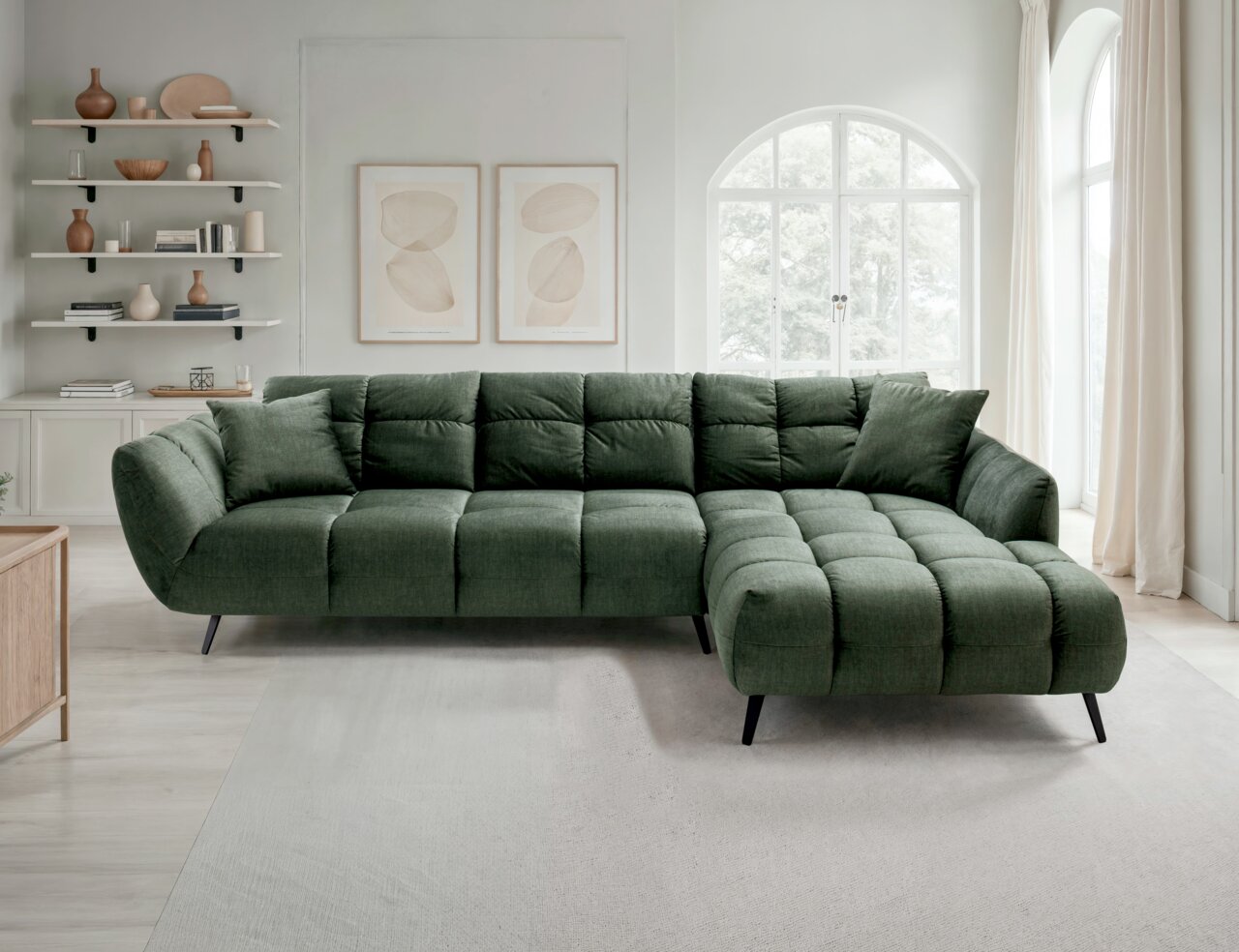 Z2 Ecksofa SALVATORE Grünes, gepolstertes Ecksofa mit Stepp-Optik und rechter Ottomane auf schwarzen Metallfüßen in hellem Wohnzimmer, Frontansicht leicht schräg von vorn.