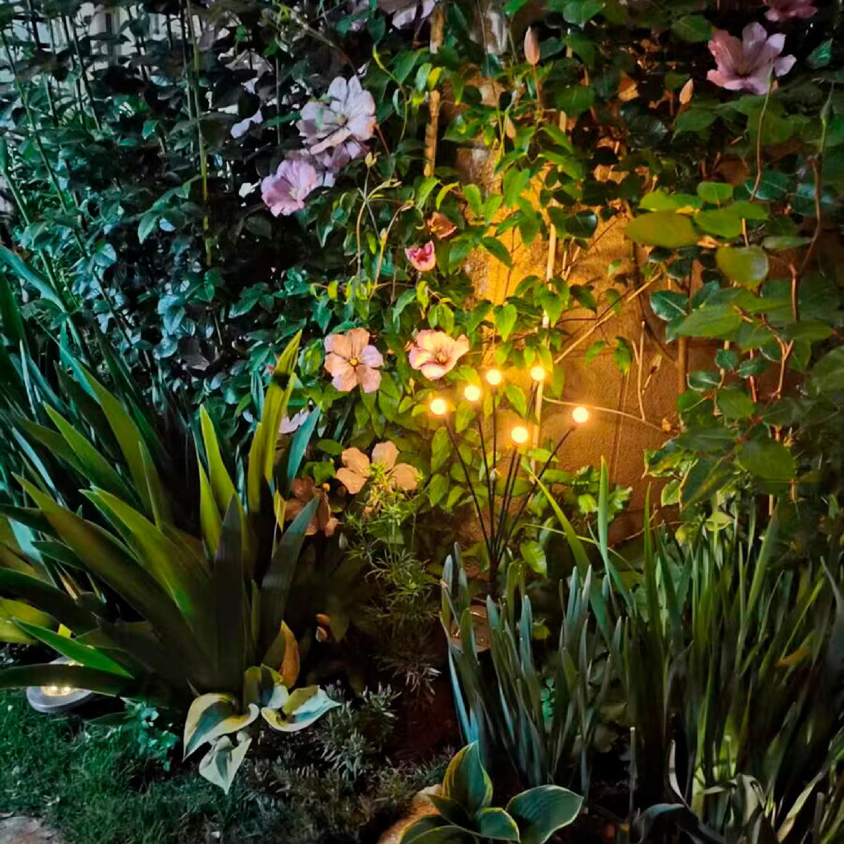 Lumineo Solar Stabbeleuchtung Solarbetriebene Stabbeleuchtung aus Plastik in einem Garten, umgeben von blühenden Pflanzen, seitliche Perspektive.