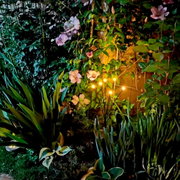 Op zonne-energie werkende stavenverlichting van kunststof in een tuin, omringd door bloeiende planten, zijaanzicht.