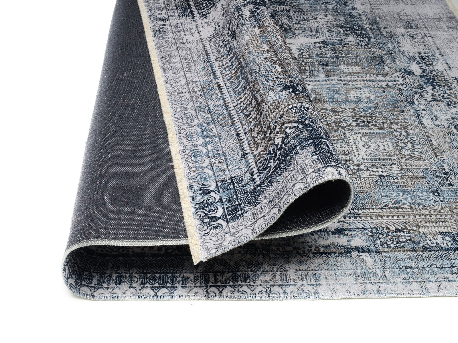 Teppich Vision Yama in Blau- und Grautönen, teilweise aufgerollt, zeigt detailliertes Muster aus der Seitenperspektive.