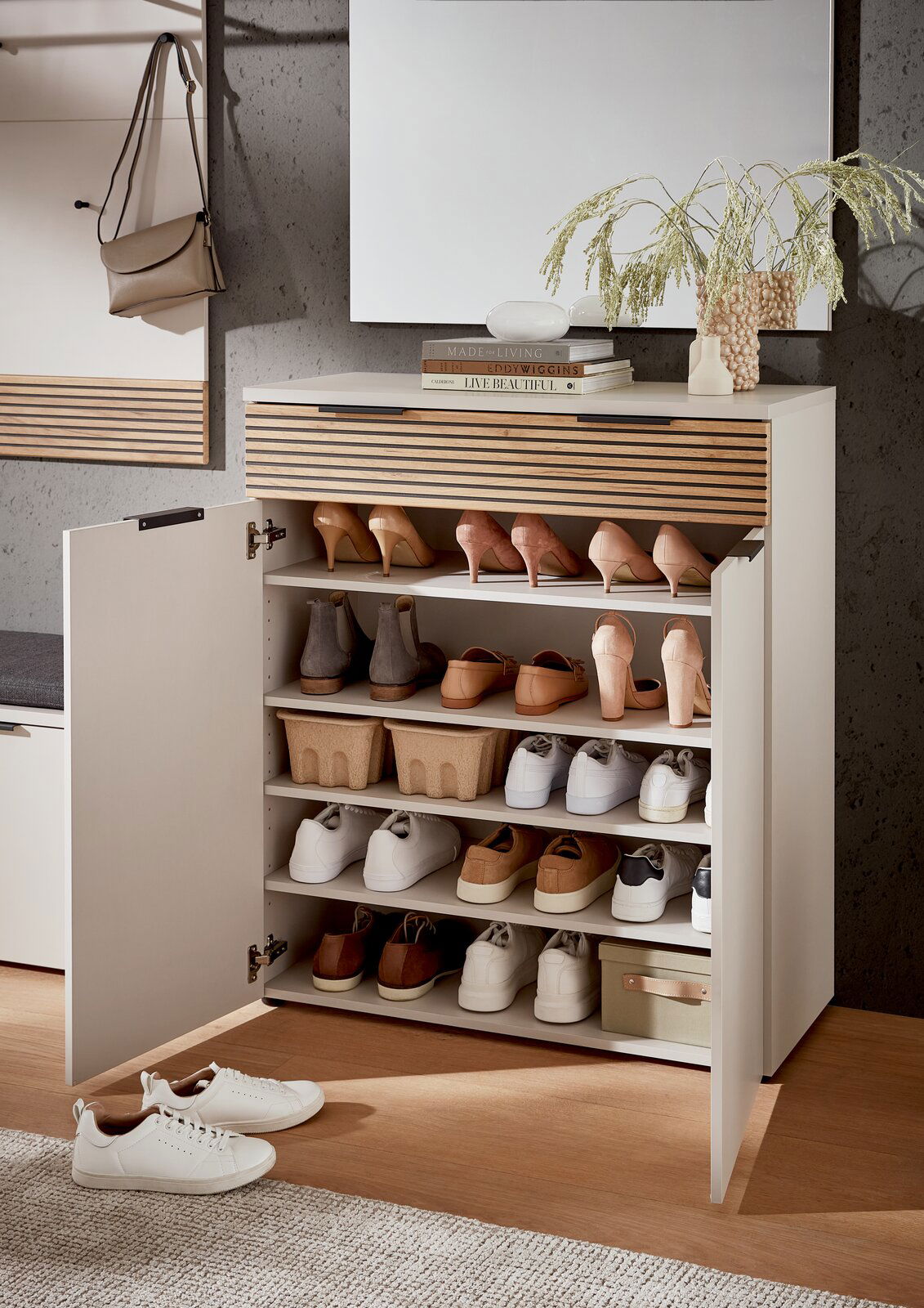 Moderner Schuhschrank mit offenen Türen, gefüllt mit verschiedenen Schuhen, aus einer frontalen Perspektive fotografiert. Auf der Oberseite des Schranks befinden sich Dekorationsgegenstände und Bücher.