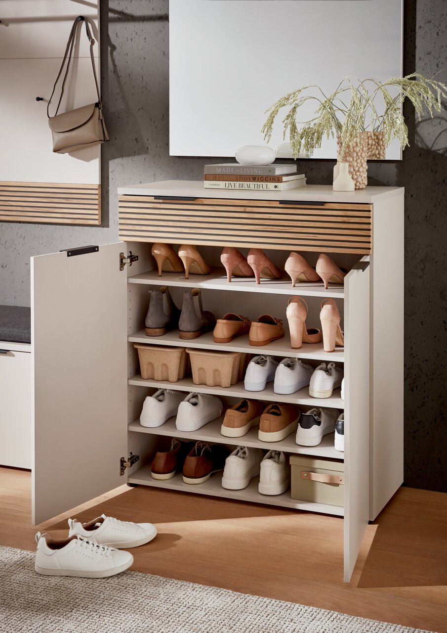 Moderner Schuhschrank mit offenen Türen, gefüllt mit verschiedenen Schuhen, aus einer frontalen Perspektive fotografiert. Auf der Oberseite des Schranks befinden sich Dekorationsgegenstände und Bücher.