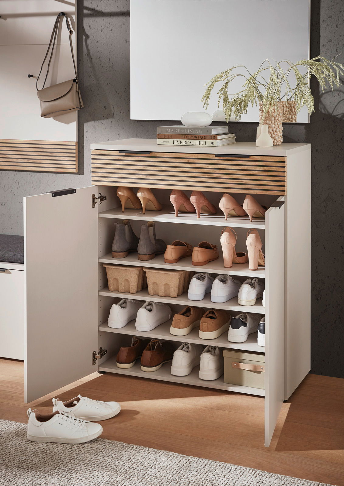 Moderner Schuhschrank mit offenen Türen, gefüllt mit verschiedenen Schuhen, aus einer frontalen Perspektive fotografiert. Auf der Oberseite des Schranks befinden sich Dekorationsgegenstände und Bücher.