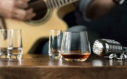 Whiskyglas Pure auf einem Holztisch, im Hintergrund eine Gitarre und ein Mikrofon, seitliche Perspektive