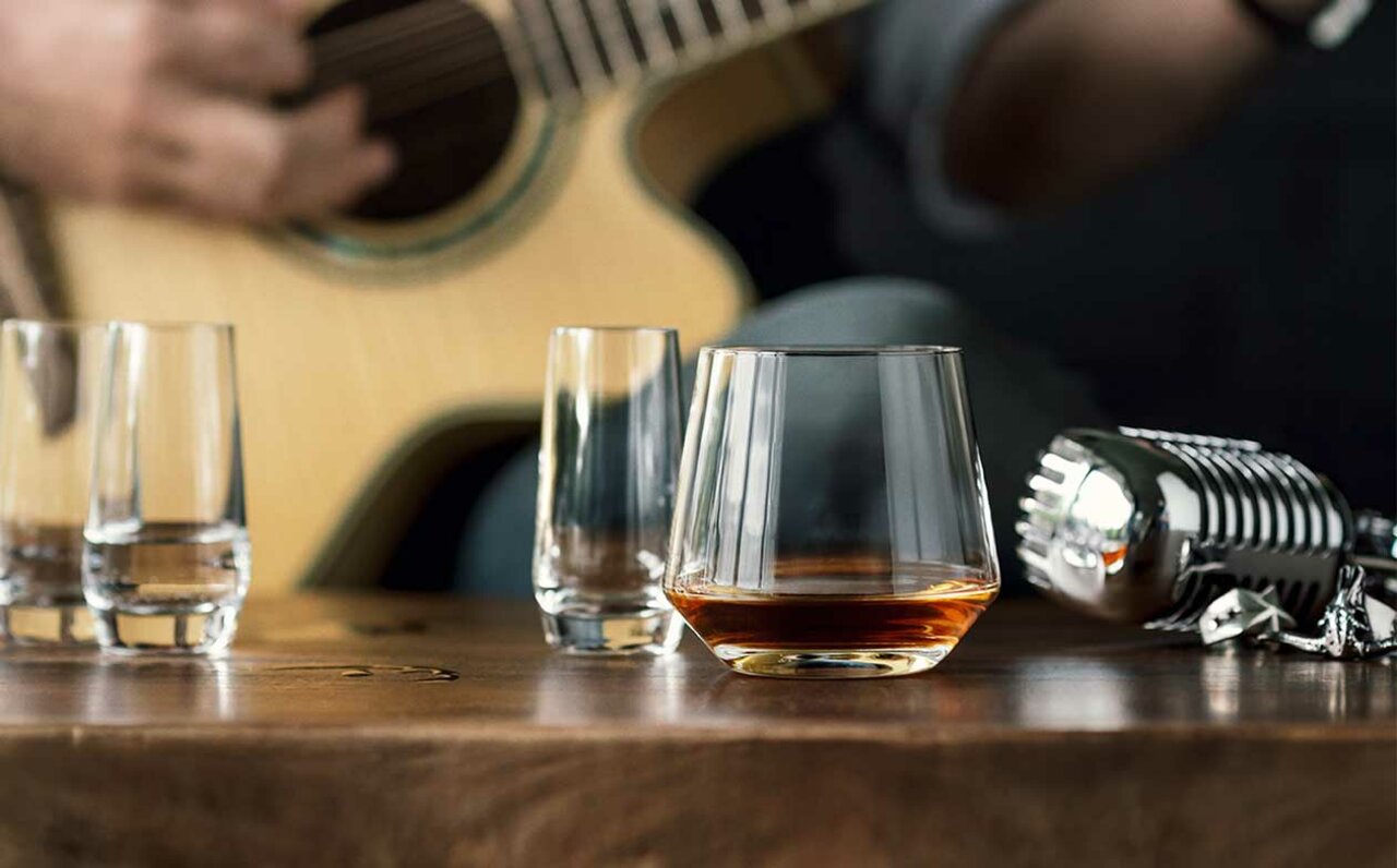 Whiskyglas Pure auf einem Holztisch, im Hintergrund eine Gitarre und ein Mikrofon, seitliche Perspektive
