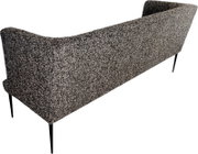 Gepolstertes Sofa mit grauem Bouclé-Bezug und schwarzen, schlanken Metallbeinen, Rückansicht in leichter Schrägperspektive von hinten