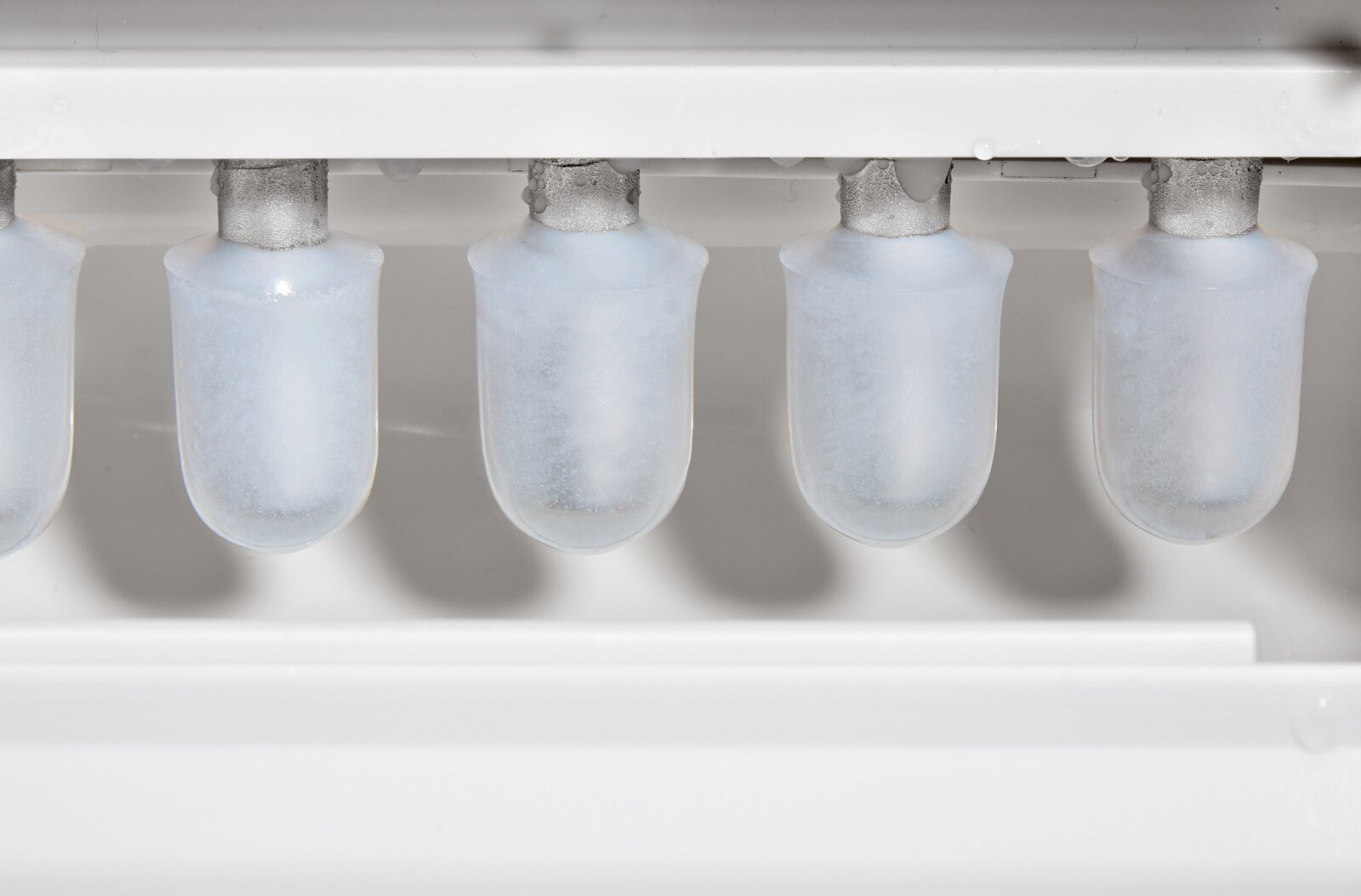 Close-up in vooraanzicht van kogelvormige ijsblokjes die in een automatische ijsblokjesmachine worden gevormd