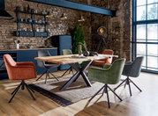 Esszimmer mit modernem Esstisch aus Holz und Metallgestell, umgeben von verschiedenen farbigen Sesseln in einem industriellen Loft-Ambiente, seitliche Perspektive.