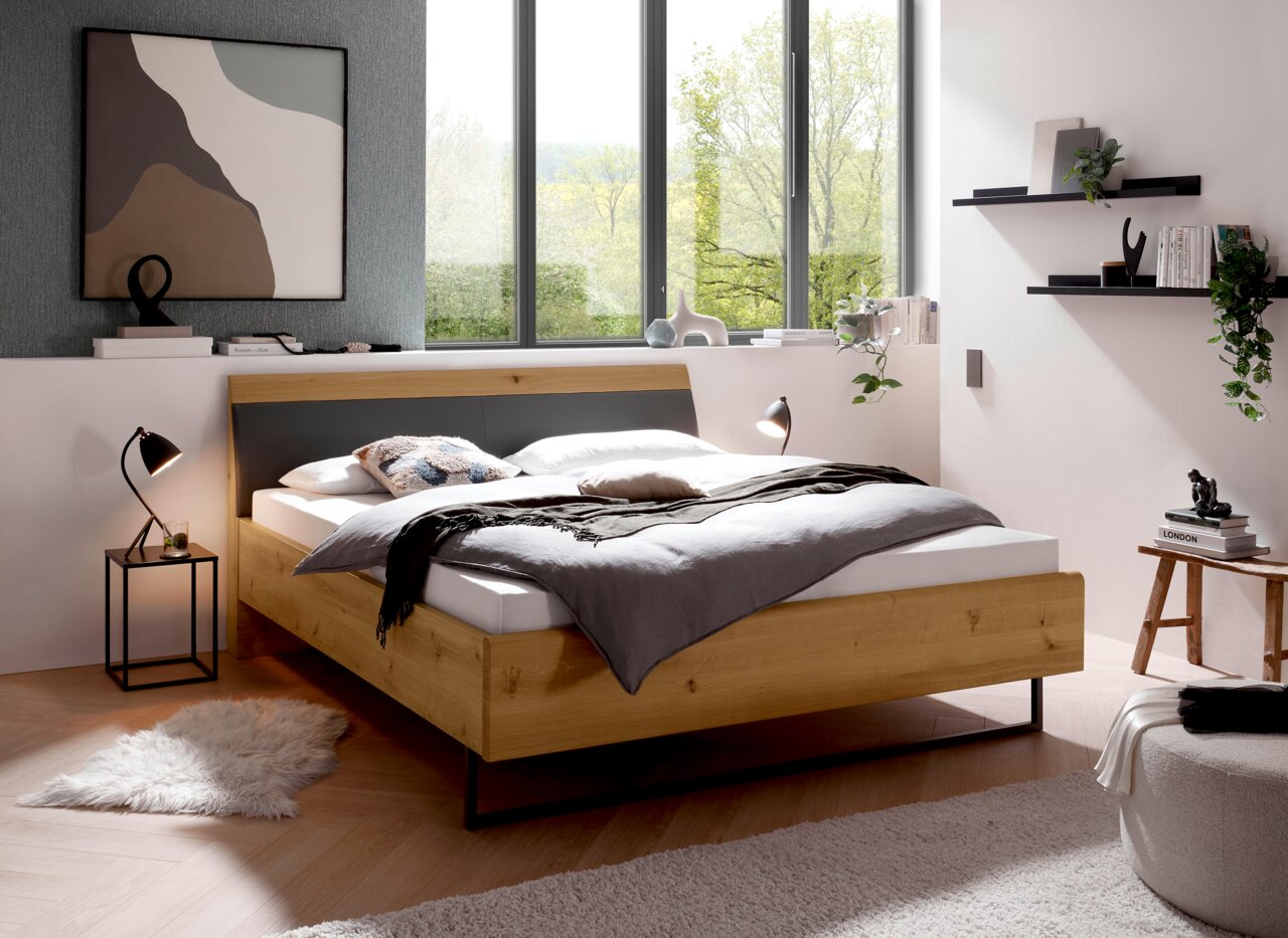 Modernes Futonbett aus Holz in einem stilvollen Schlafzimmer mit großen Fenstern, seitliche Perspektive.