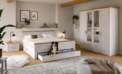 Modernes Schlafzimmer-Set in Weiß mit Holz-Akzenten: Doppelbett mit ausgezogener Bettkasten-Schublade, zwei Nachttische mit Lampen und großer Kleiderschrank mit Spiegeltüren; Ansicht schräg von vorn.