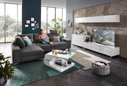 Moderne Wohnzimmermöbel in einem hellen Raum mit großen Fenstern, bestehend aus einem grauen Ecksofa, einem weißen Funktions-Couchtisch und einem weißen TV-Lowboard. Perspektive von vorne.