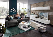 Moderne Wohnzimmermöbel in einem hellen Raum mit großen Fenstern, bestehend aus einem grauen Ecksofa, einem weißen Funktions-Couchtisch und einem weißen TV-Lowboard. Perspektive von vorne.