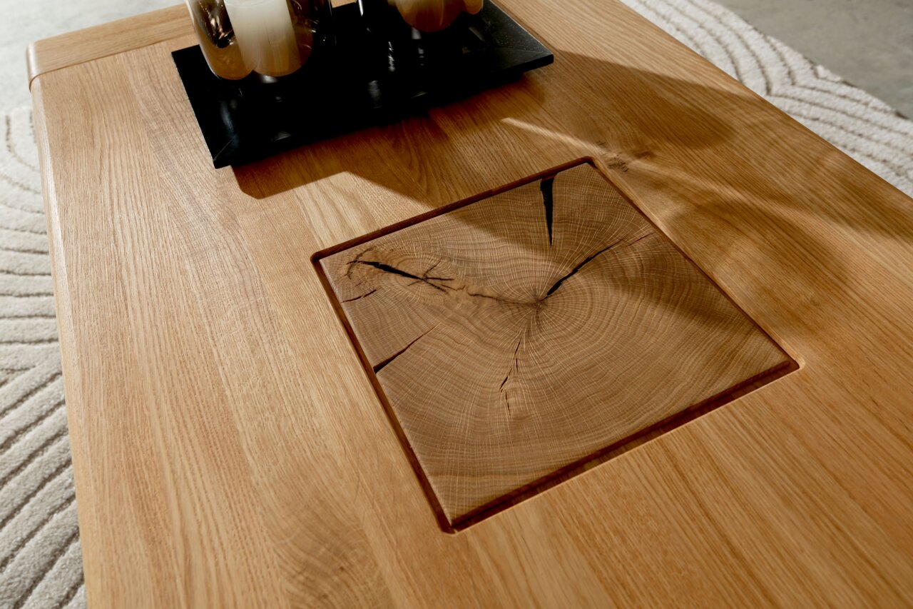 Detailaufnahme eines hellen Holztisches mit eingelassener quadratischer Holzintarsie mit sichtbaren Jahresringen und Rissen, fotografiert aus schräger Draufsicht