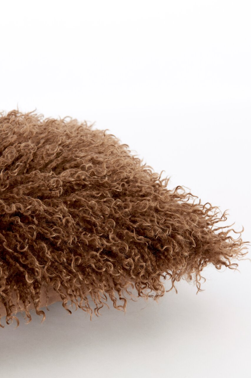 Close-up van een bruin, donzig kussen met een gekrulde textuur.