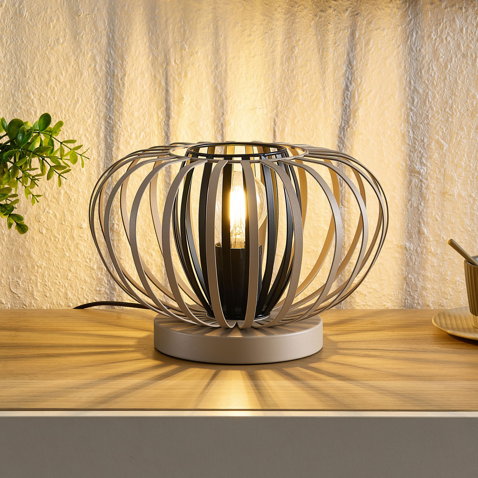 Moderne Tischleuchte mit kugelförmigem, offenen Metallrahmen, warmes Licht abstrahlend, seitliche Perspektive.