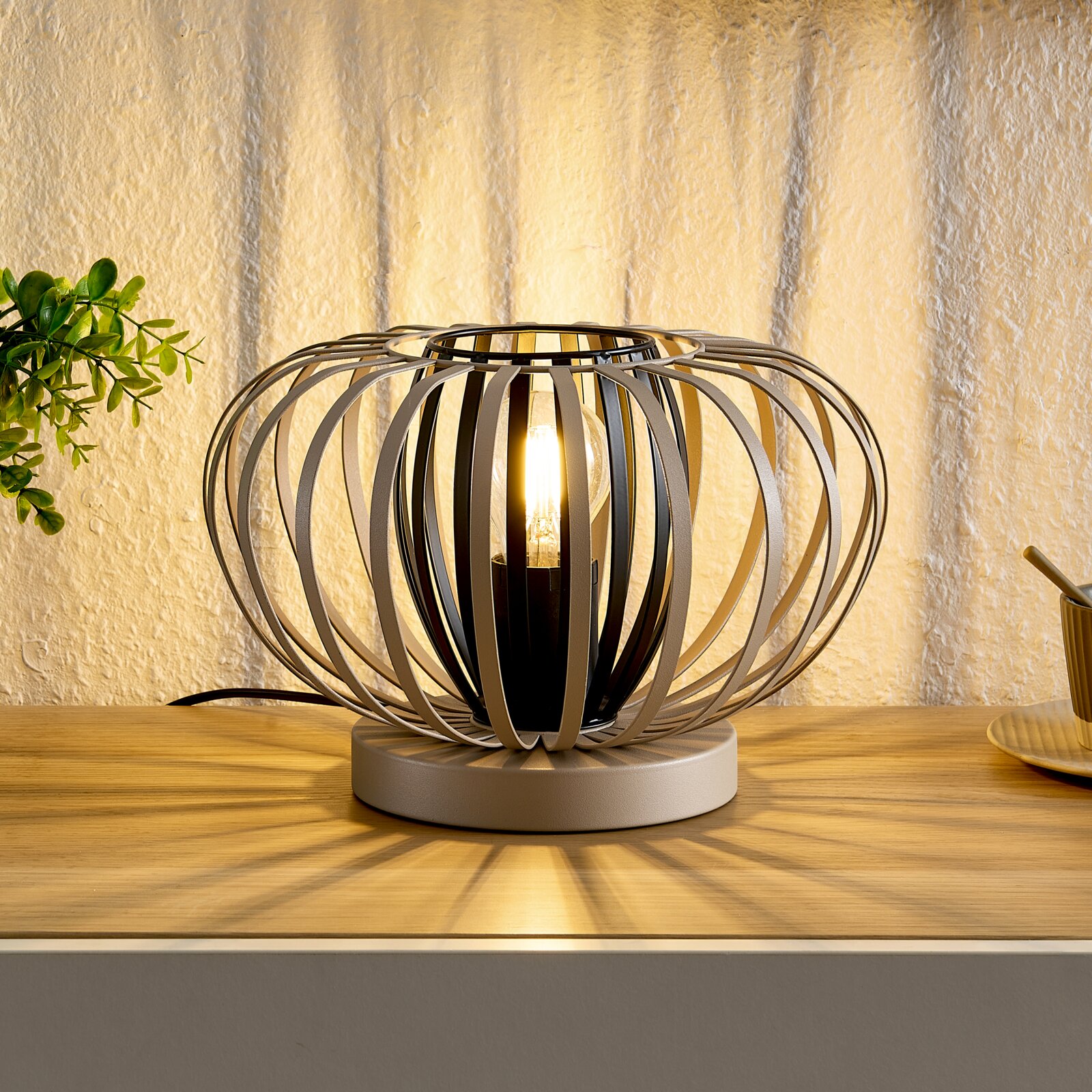 Moderne tafellamp met een bolvormig, open metalen frame, die warm licht verspreidt, gezien vanaf de zijkant.