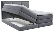 Graues gepolstertes Boxspringbett mit weißem Topper und hochgeklappter Liegefläche, die den integrierten Bettkasten zeigt, in schräger Frontansicht