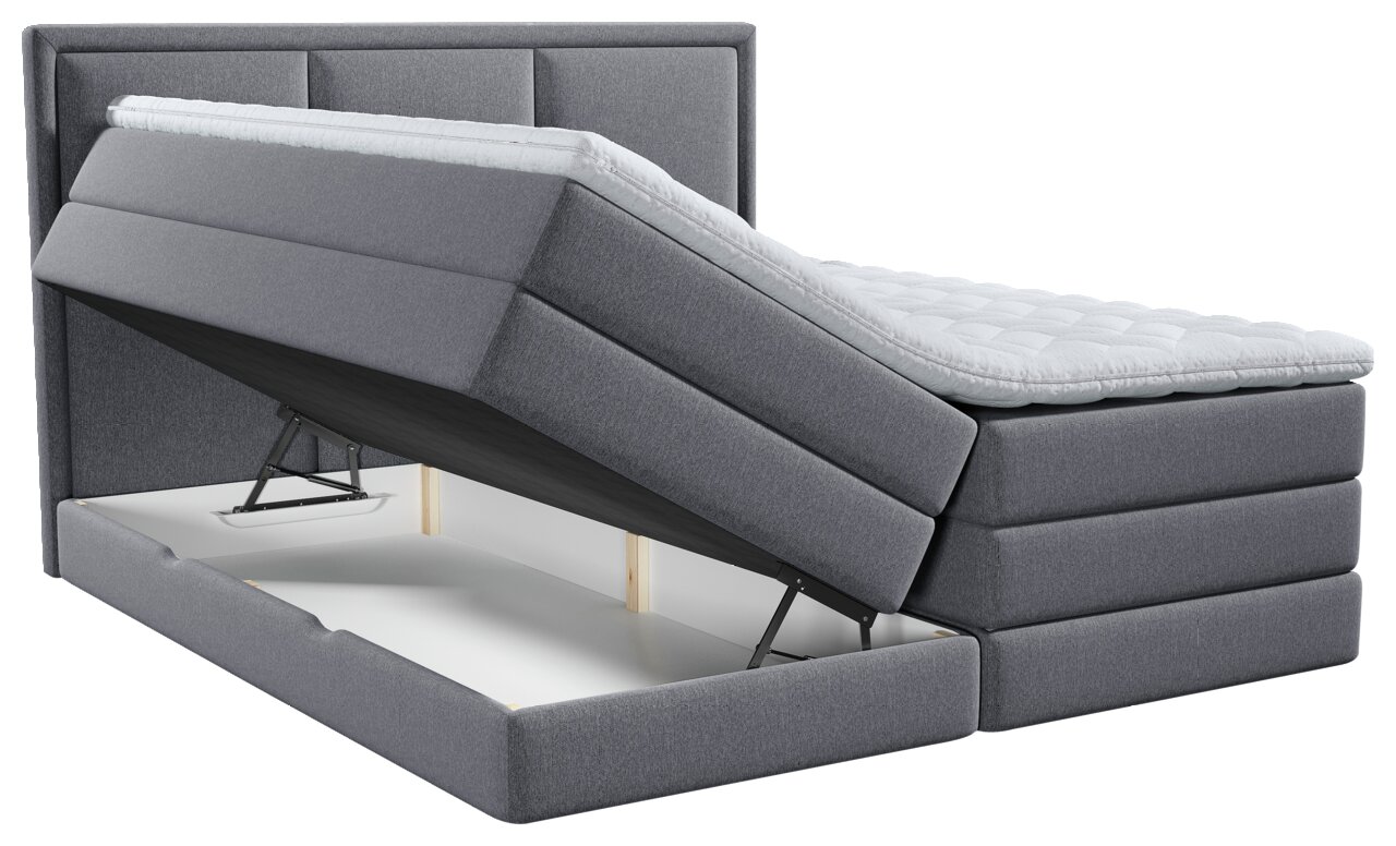 Graues gepolstertes Boxspringbett mit weißem Topper und hochgeklappter Liegefläche, die den integrierten Bettkasten zeigt, in schräger Frontansicht