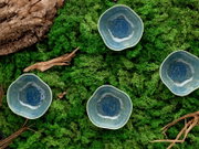 Draufsicht auf vier unregelmäßig geformte, blau glasierte Keramikschälchen auf grünem Moos mit Rindenstücken und Holzresten.