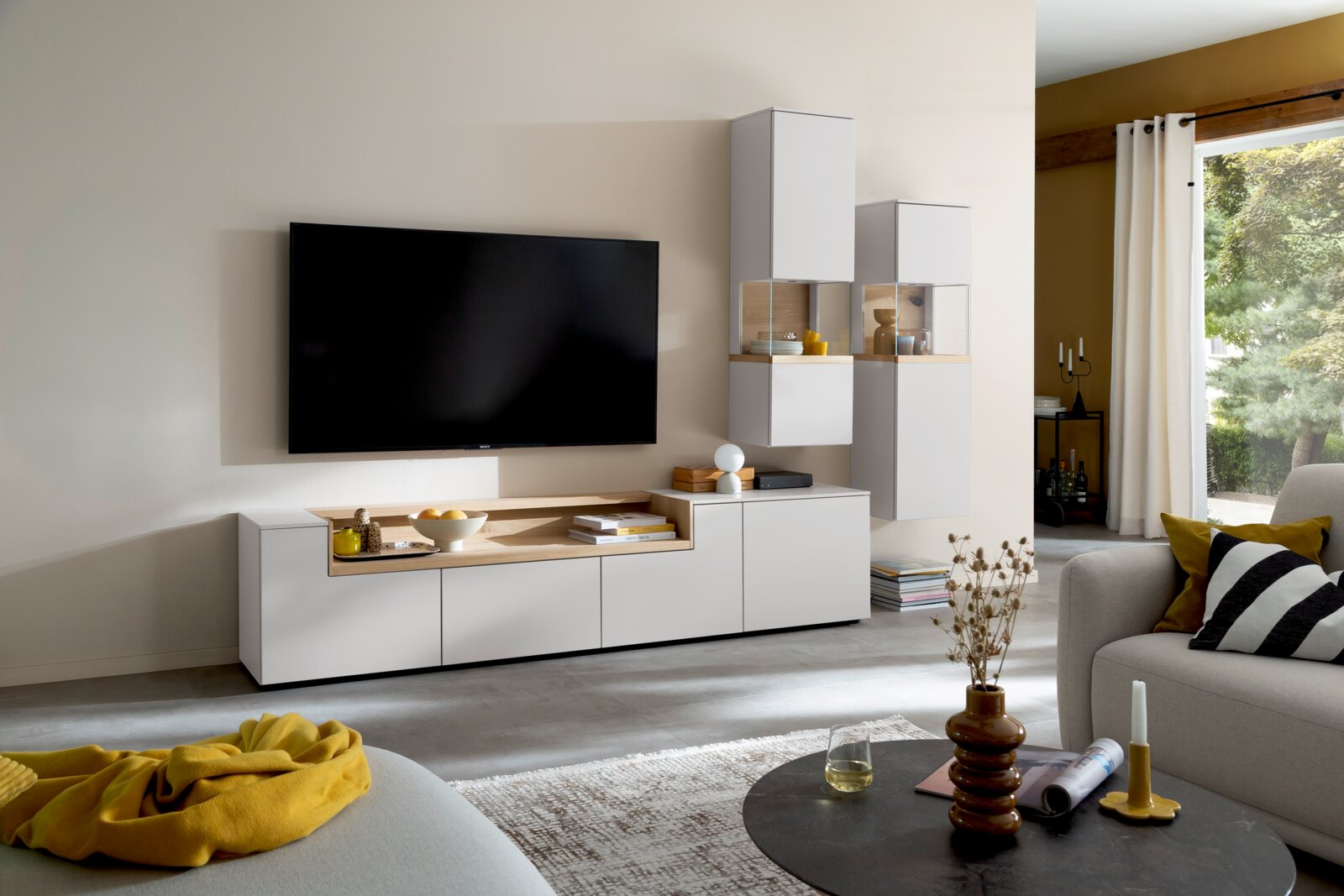 Moderne witte tv-wandmeubelcombinatie met houten accent en vitrinekasten, frontaal perspectief in een lichte woonkamer met wandgemonteerde tv.