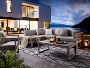 Modernes Lounge-Set auf einer Terrasse mit Blick auf einen See bei Sonnenuntergang, seitliche Perspektive.