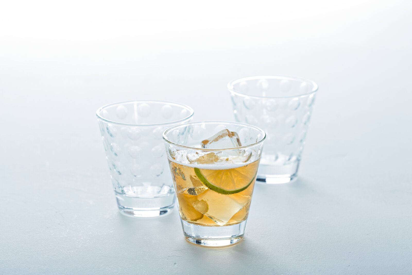 Drei Trinkgläser Optic 215ml, eines gefüllt mit einem Getränk und Eiswürfeln, aus der Vorderansicht fotografiert.