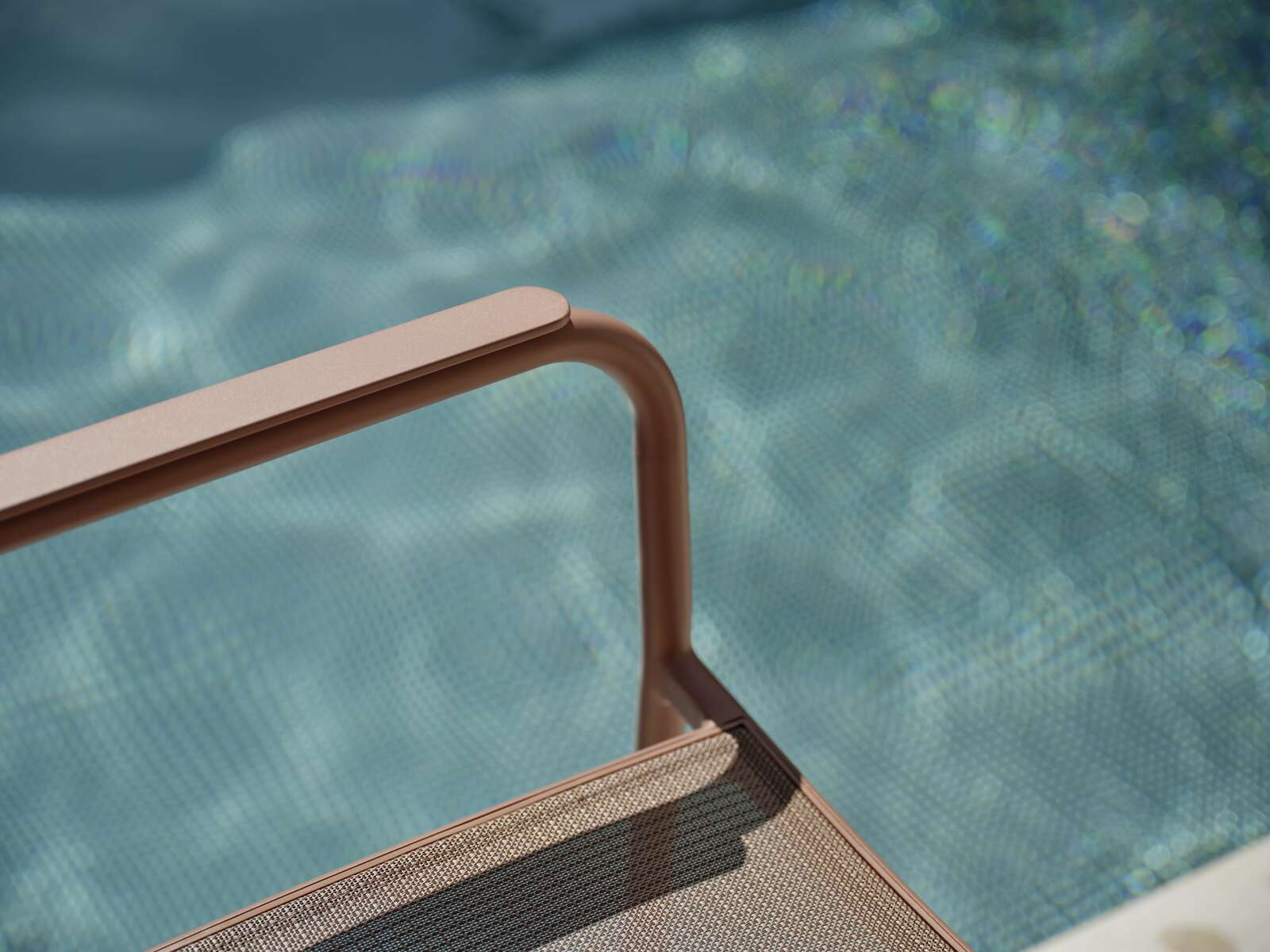 Nahaufnahme eines Stapelsessels mit Armlehne, im Hintergrund ein verschwommener Pool.