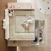 Vogelperspektive auf einen Wickelaufsatz mit weicher, gemusterter Auflage, umgeben von Spielzeug und Babyutensilien.