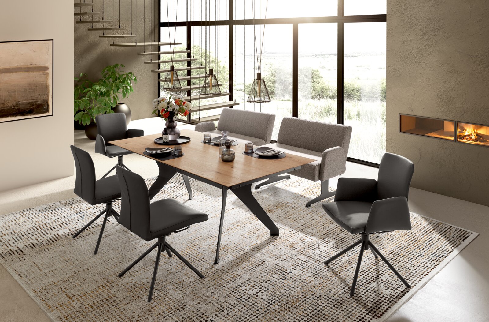Modernes Esszimmer-Set mit rechteckigem Holztisch auf schwarzem Metallgestell, vier schwarzen Drehstühlen und zwei grauen Polsterbänken auf hellem Teppich, fotografiert aus schräger Vorderansicht.