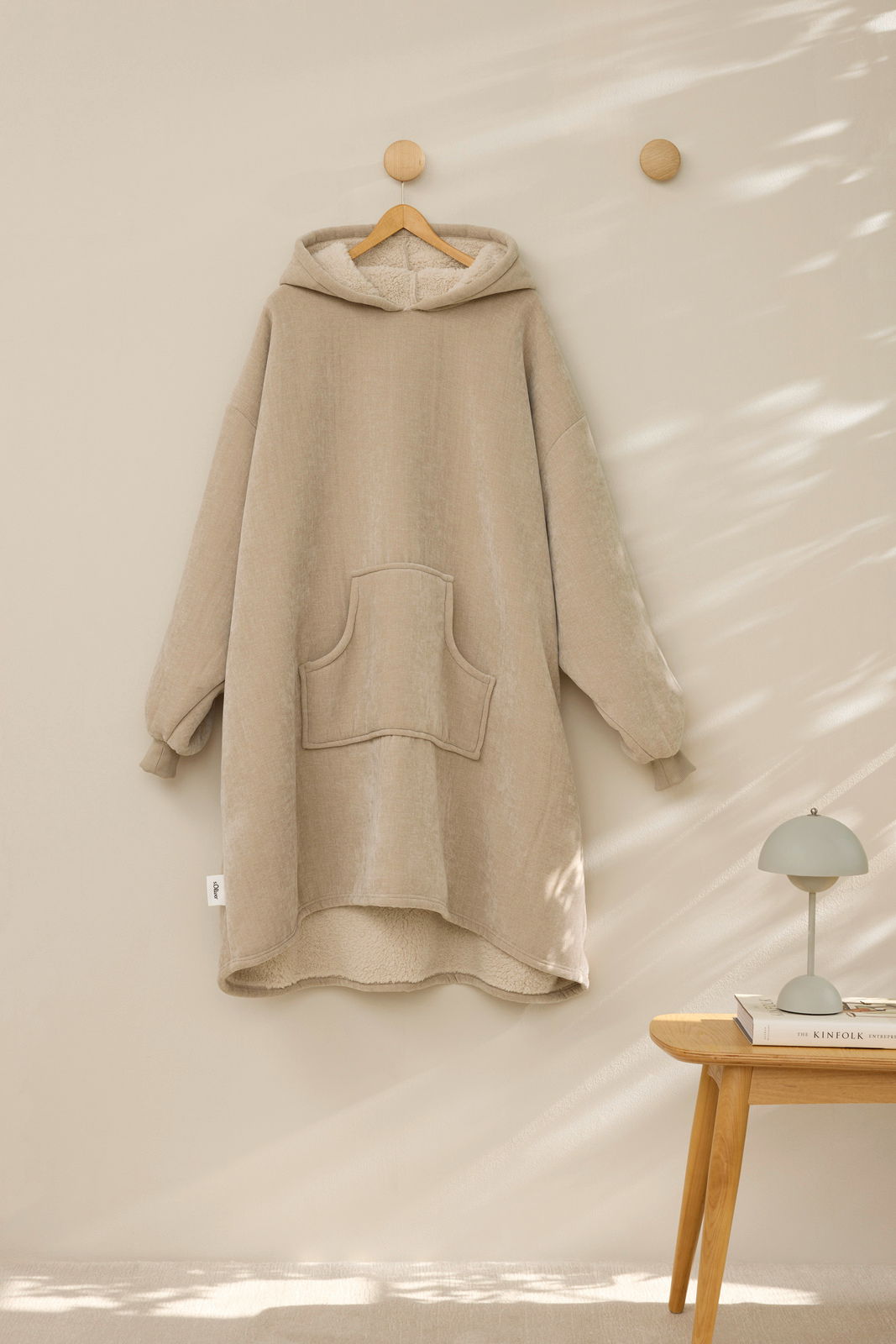s.Oliver Lounge Hoodie Beiger Lounge Hoodie mit Kapuze und Kängurutasche, frontal an der Wand hängend, mit weichem Innenfutter.
