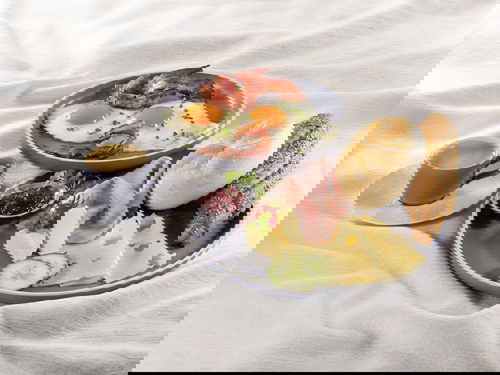 Frühstücksteller mit Spiegelei, Speck, Käse, Aufschnitt, Brötchen und Kaffee.