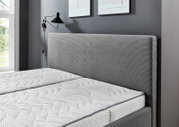 Graues Polsterbett 160x200 mit gestreiftem Kopfteil, seitliche Perspektive, modernes Schlafzimmerdesign.