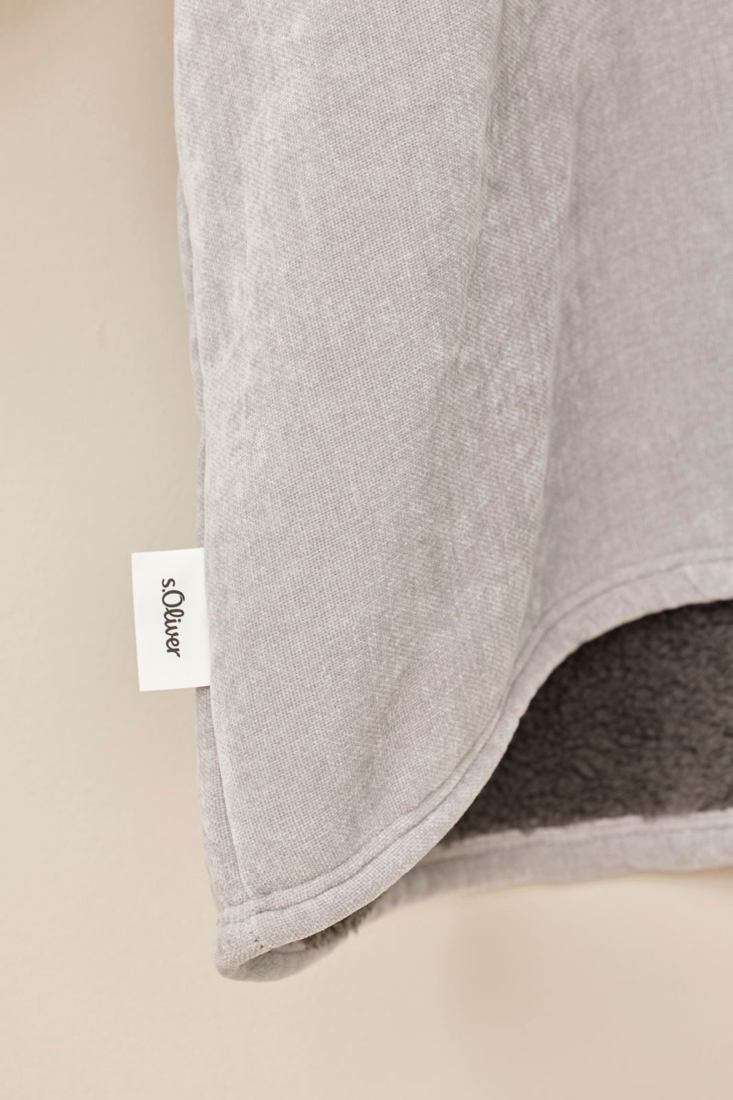 Nahaufnahme eines grauen Lounge Hoodies mit weichem Innenfutter und sichtbarem Markenetikett, seitliche Perspektive.