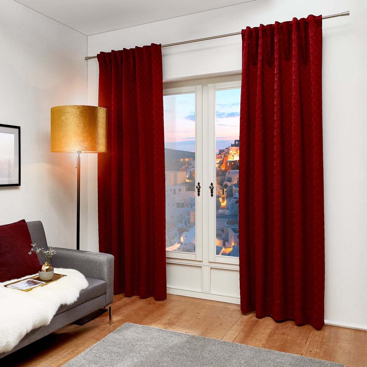 Roter Dekoschal J!Fina 130x250 cm, frontal vor einem Fenster in einem gemütlichen Wohnzimmer mit grauem Sofa und Stehlampe.