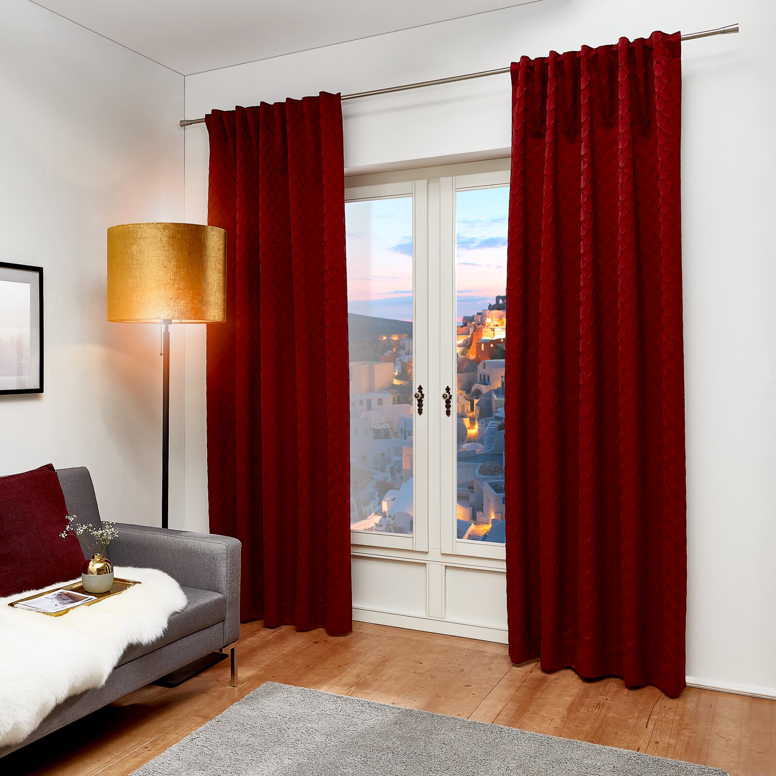 JOOP! Dekoschal 140x250cm J!FINA Roter Dekoschal J!Fina 130x250 cm, frontal vor einem Fenster in einem gemütlichen Wohnzimmer mit grauem Sofa und Stehlampe.