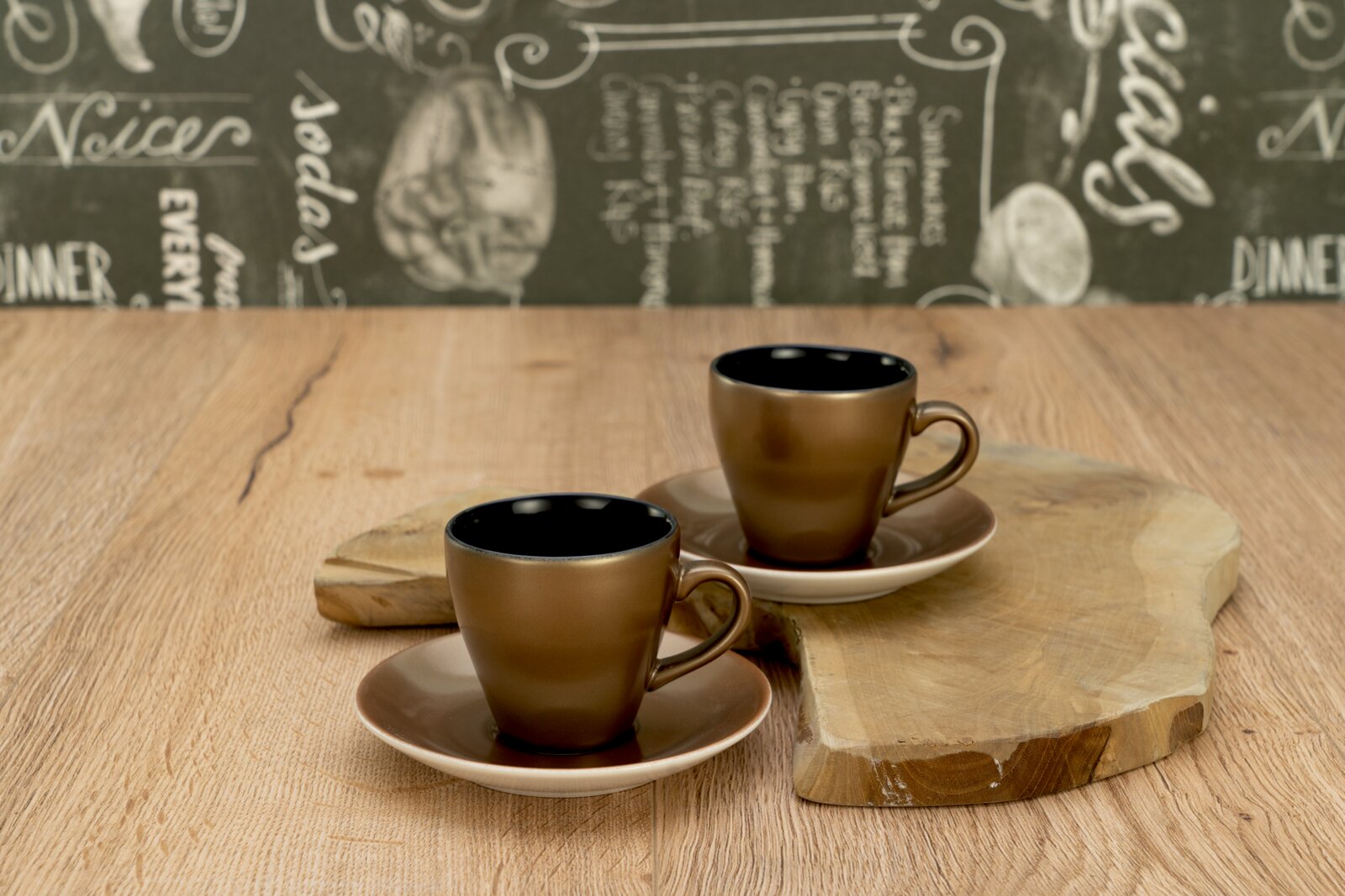 Zwei braune Keramik-Espressotassen mit Untertassen auf einem Holzbrett auf Holztisch, fotografiert aus leicht erhöhter Frontperspektive