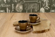 Zwei braune Keramik-Espressotassen mit Untertassen auf einem Holzbrett auf Holztisch, fotografiert aus leicht erhöhter Frontperspektive