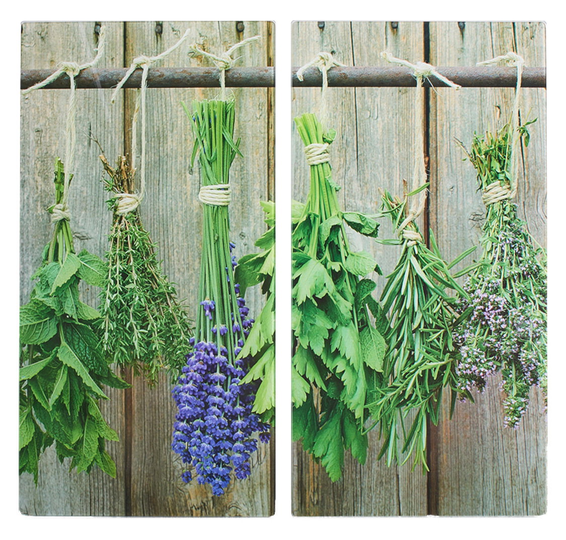 Zwei Herdabdeck- und Schneideplatten mit einem Motiv von hängenden Kräuterbündeln vor einem rustikalen Holzhintergrund, aus der Vorderansicht fotografiert.