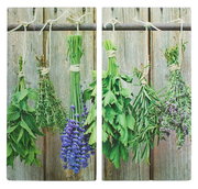 Zwei Herdabdeck- und Schneideplatten mit einem Motiv von hängenden Kräuterbündeln vor einem rustikalen Holzhintergrund, aus der Vorderansicht fotografiert.