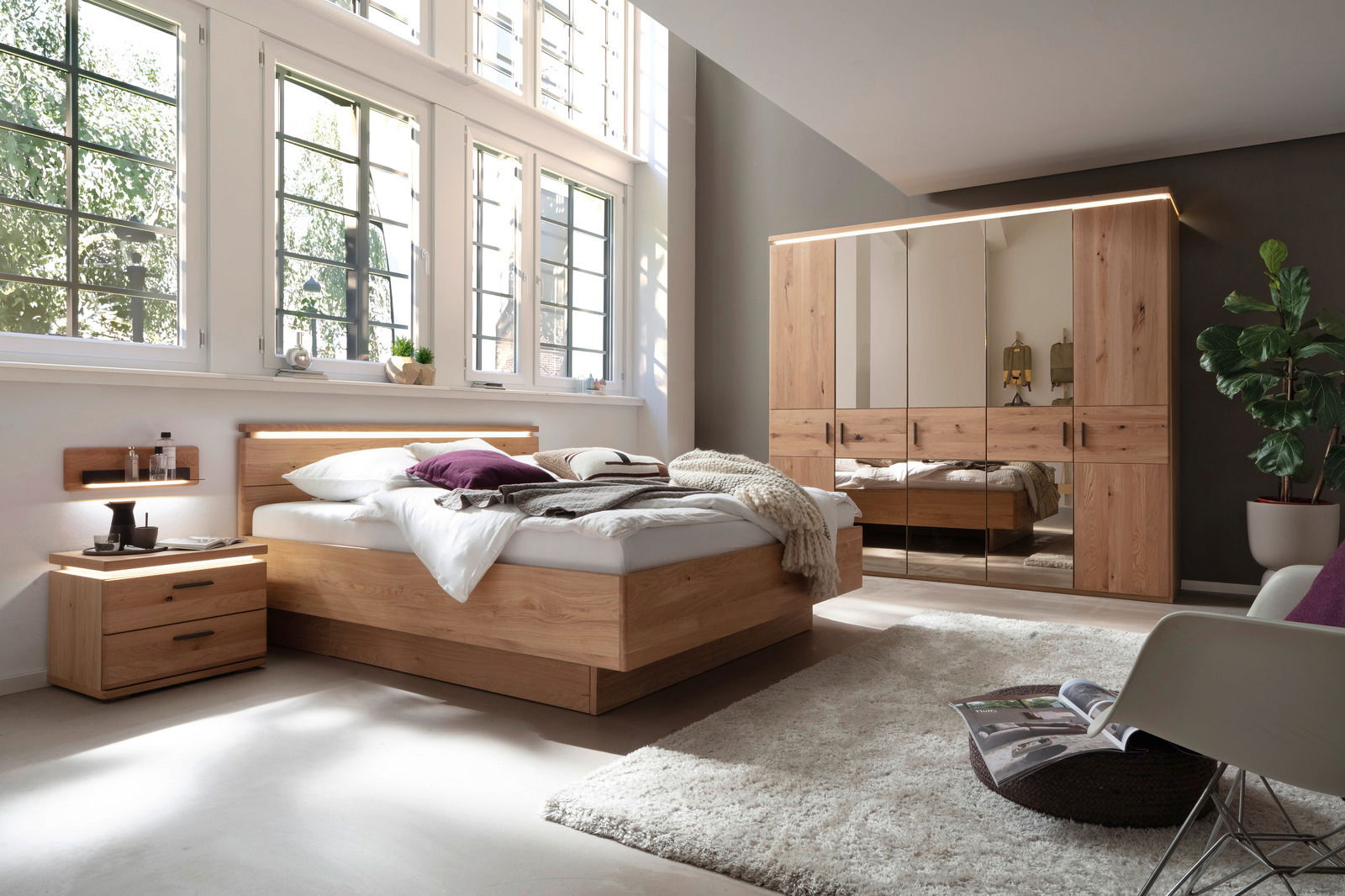 Helles Schlafzimmer mit einem fünftürigen Drehtürenschrank, einem Bett mit Holzrahmen, einer Nachtkonsole und einem Wandboard. Die Perspektive zeigt den Raum von der Seite, mit großen Fenstern, die viel Licht hereinlassen.