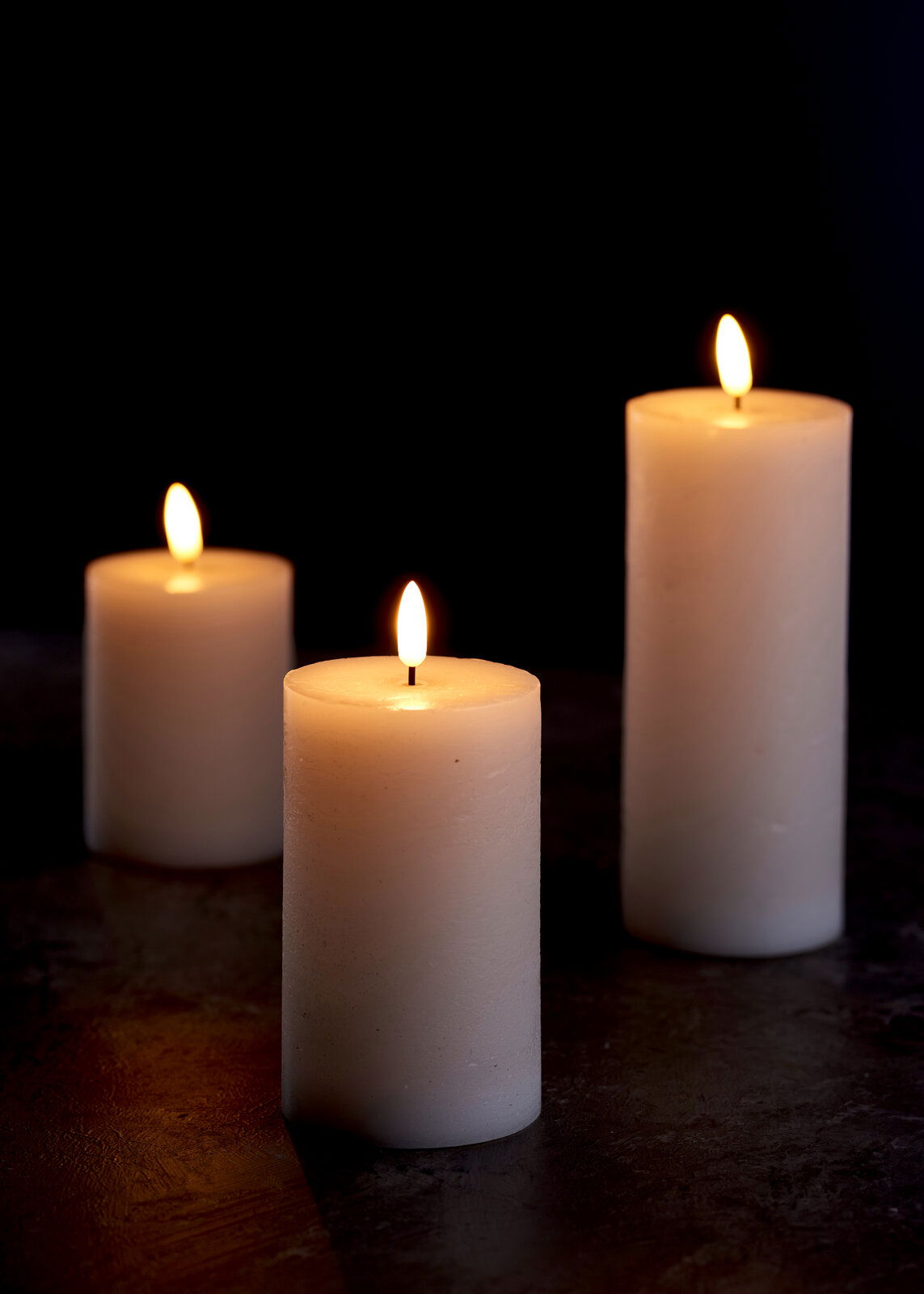 Drei weiße 3D-LED-Kerzen mit flackernder Flamme auf dunklem Hintergrund, aus seitlicher Perspektive fotografiert.
