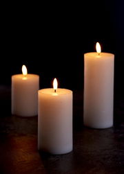 Drei weiße 3D-LED-Kerzen mit flackernder Flamme auf dunklem Hintergrund, aus seitlicher Perspektive fotografiert.