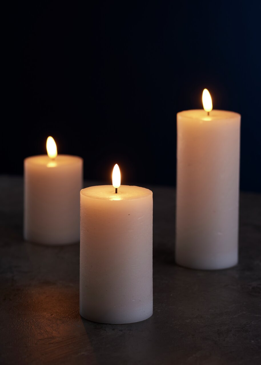 Drei weiße 3D-LED-Kerzen mit flackernder Flamme auf dunklem Hintergrund, aus seitlicher Perspektive fotografiert.