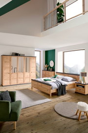 Schlafzimmer mit Holzmöbeln, bestehend aus einem großen Bett, einem Kleiderschrank mit Spiegeltüren und einer Nachtkommode, aus der Perspektive von vorne rechts betrachtet.