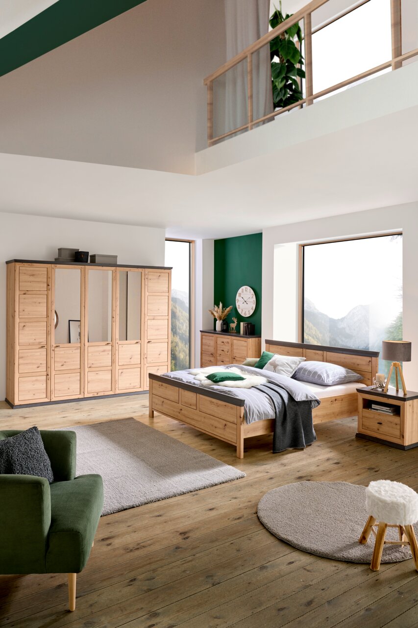 Schlafzimmer mit Holzmöbeln, bestehend aus einem großen Bett, einem Kleiderschrank mit Spiegeltüren und einer Nachtkommode, aus der Perspektive von vorne rechts betrachtet.