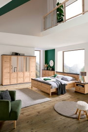 Schlafzimmer mit Holzmöbeln, bestehend aus einem großen Bett, einem Kleiderschrank mit Spiegeltüren und einer Nachtkommode, aus der Perspektive von vorne rechts betrachtet.