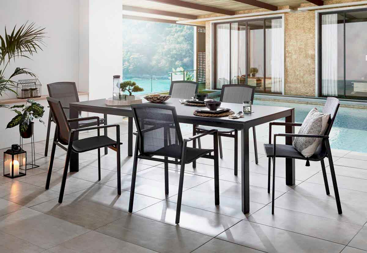 Modernes Outdoor-Esszimmer-Set mit rechteckigem grauem Gartentisch und sechs passenden Stühlen mit Netzbespannung auf einer überdachten Terrasse am Pool, Perspektive: leicht seitliche Frontansicht auf Tisch und Stühle