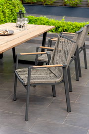 Moderner Stapelsessel mit Metallrahmen und geflochtener Sitzfläche, seitliche Perspektive neben einem Holztisch im Garten.