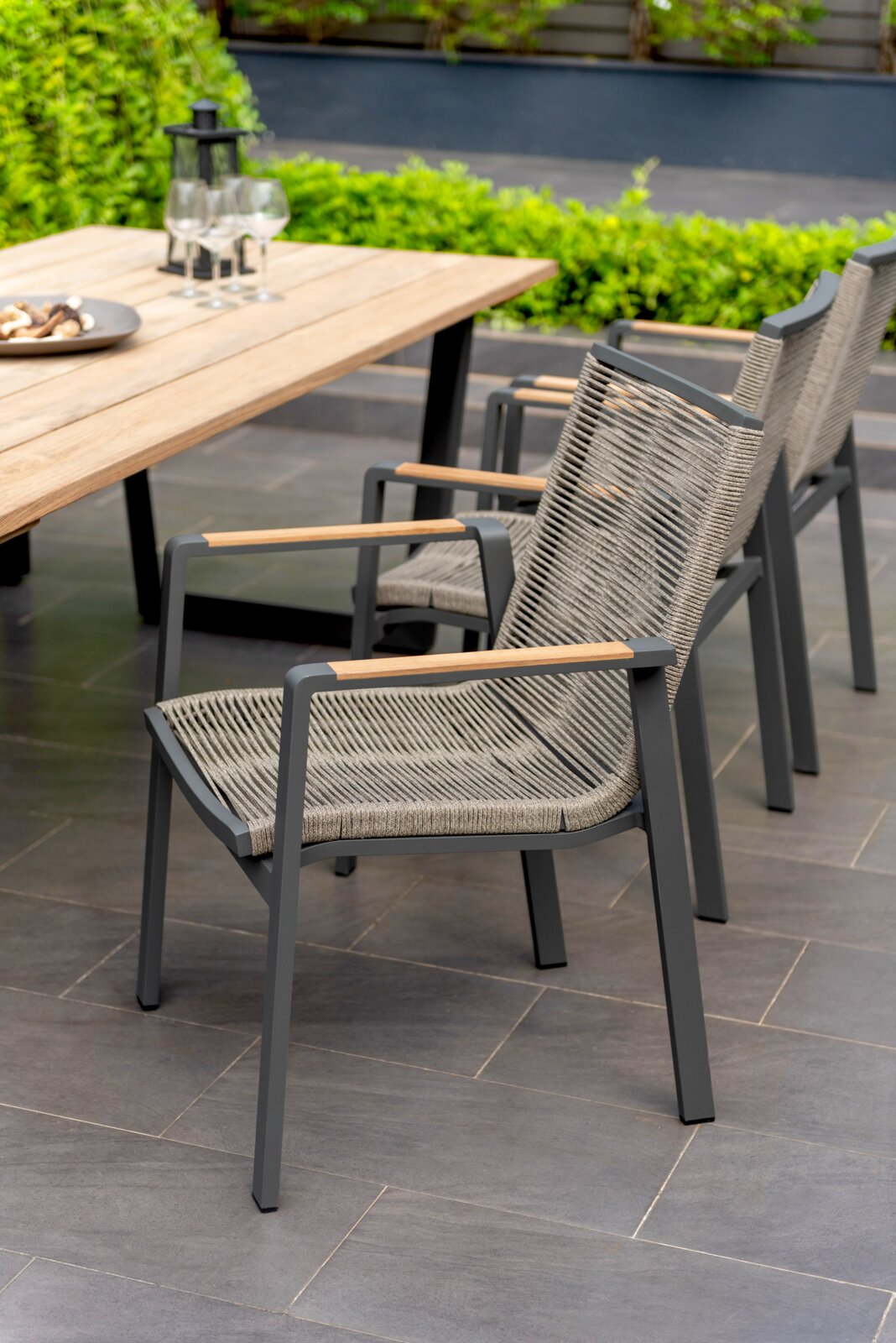 Moderne stapelstoel met metalen frame en gevlochten zitting, zijaanzicht naast een houten tafel in de tuin.